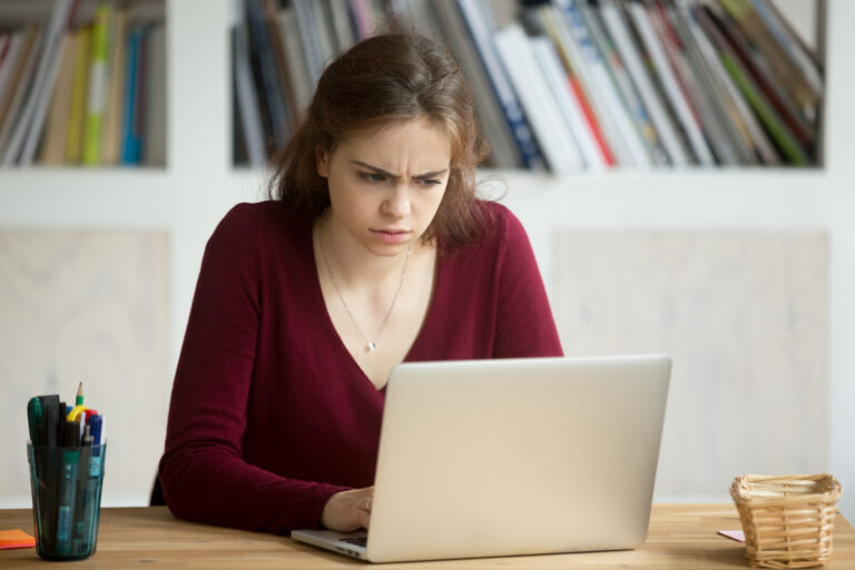 Perplexed young casual female entrepreneur looking at laptop screen.